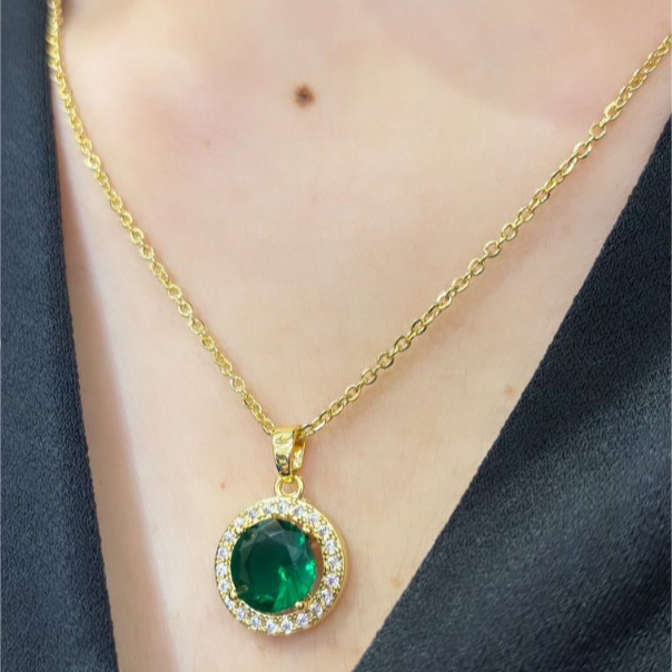 A stainless steel emerald locket necklace with a gold chain and a circular green pendant on a person's neck.